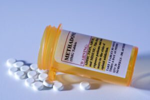 Tipped over orange prescription bottle with methadone pills spilling out.